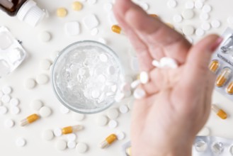 Hand pouring white tablets into a glass with water on a light background