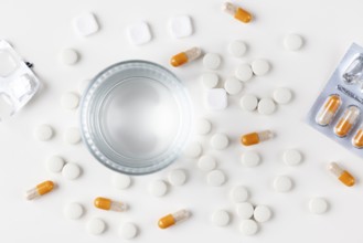 Glass of water with tablets and orange-white capsules on a white background
