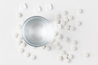 Glass of water with lots of scattered white tablets on a white surface