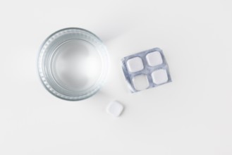 Glass of water with packaging and tablets on a white surface