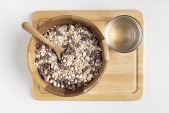 Rustic bowl with cereal and wooden spoon on a wooden board, water glass next door