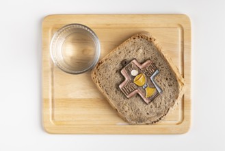 Bread with cross symbol on a wooden board with a glass of water next to it, white background