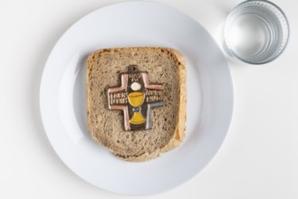 A slice of bread with a cross symbol on it, water next to it, fasting