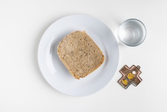 Slice of bread on a plate with a water glass and a cross symbol on a plain white background,