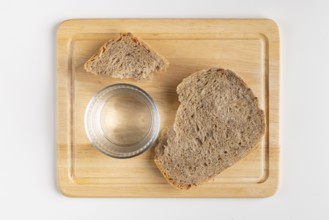 Wooden board with a large and a small piece of bread and a glass of water