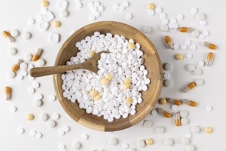 Wooden bowl filled and surrounded by tablets and capsules on light background
