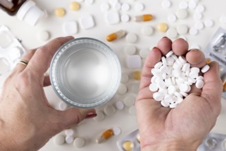 Two hands hold a glass of water and a handful of tablets across a table