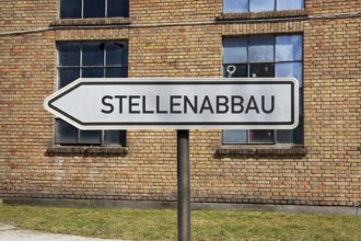 (photo montage) Directional arrows with the inscription JOB REDUCTION in front of an old industrial