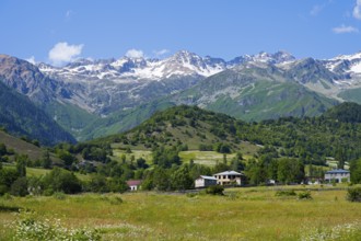 Picturesque mountain landscape with snowy peaks, green hills and meadows under blue skies,