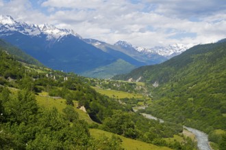 Extensive mountain landscape with river in the valley and lush green forests under blue sky,