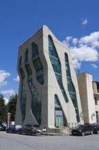 Modern, futuristic building with wavy glass facades and cars in front of it, police station