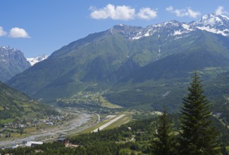 Valley with river and adjacent mountains under a bright blue sky, in the middle an airport, Mestia,