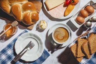 Breakfast with toast, stollen, honey, cheese, ham, coffee, butter, peppers and eggs on a table