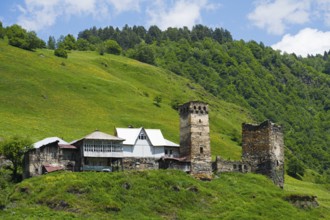 Medieval village with tower on a hill in the background, surrounded by green landscape and clear