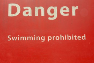 Danger Swimming Prohibited in white letters on red painted metal public notice sign in public park,