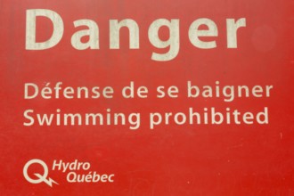 Bilingual French and English Danger Swimming Prohibited in white letters on red painted metal