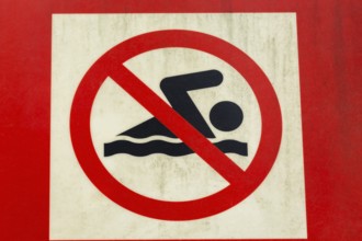 Close-up of posted painted red and white with illustrated swimmer in solid black on metal pictogram