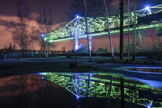 Green-lit bridge structure at night reflecting in a water surface, Landschaftspark Duisburg Nord,