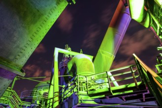 Detailed view of a metallic industrial plant illuminated with green and purple lights,