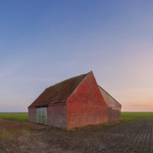 View of a rural building made of baked stone standing in a field at sunset, Aschwarden,