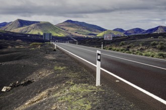 Empty road leads through a volcanic mountain landscape under cloudy sky, Yaiza Lanzarote