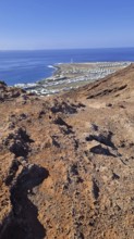 View from a rocky volcanic mountain (Montana Roja) to the distance and the blue sea, Playa Blanca