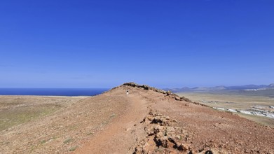 Narrow path on the summit of the Montana Roja volcano with views of the sea under a clear blue sky,