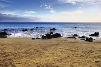 Peaceful sandy beach with rocks and calm sea under a wide sky, Puerto del Carmen Lanzarote