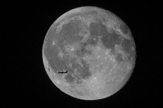 Silhouette of a passenger plane flying in front of a huge and brightly lit full moon with