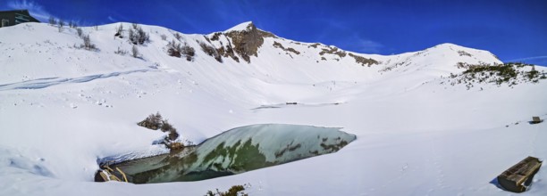 Alpine mountain panorama in snow on Schlappoldsee with wooden bench on Fellhorn in spring in the