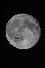 Silhouette of a passenger plane flying in front of a huge and brightly lit full moon with