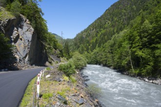 Mountain road next to a flowing river in a green, wooded landscape in clear summer weather, Enguri