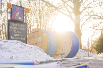 Sun rays fall on cable rolls next to a construction site sign surrounded by snow, fibreglass
