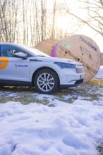 A car stands next to large rolls of cable on a snow-covered meadow in winter, fibreglass