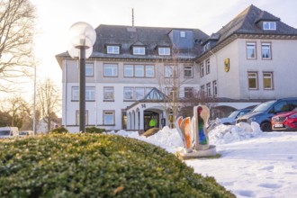 A snowy building with sculptures and parked cars in winter light, fibreglass groundbreaking,