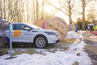 A car is parked next to large cable drums in a wintry environment with construction work,