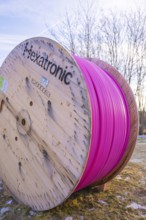 A large pink cable reel stands in a meadow under a blue sky in winter, fiberglass groundbreaking,