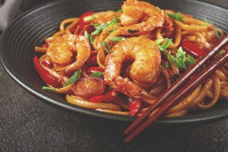 Udon stir-fry shrimp noodles with red bell pepper and green onion, served in a black bowl, with