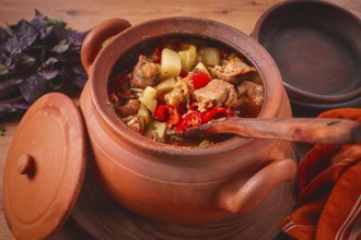 Chanakhi, a Georgian dish. in a clay pot, on a wooden table, stewed meat with vegetables, homemade,