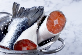 Fish tails are placed in a colander on a marble counter. The colander allows water to drain away
