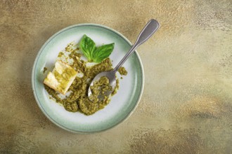 On a platter is a pesto sauce made from fresh basil, with a slice of bread and a spoon on a plate.