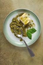On a platter is a pesto sauce made from fresh basil, with a slice of bread and a spoon on a plate.