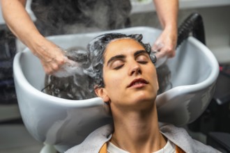 Young woman relaxing with closed eyes while hairdresser hands gently wash her hair with shampoo and