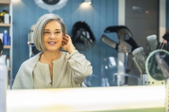 Senior woman looking at her reflection in the salon mirror, smiling and admiring her new short