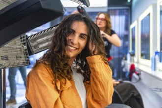 Woman with curly hair smiling while receiving hair drying and treatment at a modern hair salon,