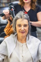 Mature woman sitting in a hair salon during a blow dry session, smiling confidently while a