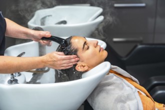 Woman relaxed in salon basin as hairstylist rinses shampoo and massages scalp with warm water and