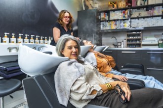 Two women reclining at salon basins while a stylist performs professional shampoo and scalp care,