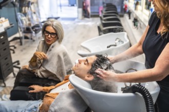 Professional hairdresser washing a young client's hair at the shampoo basin, providing hair care