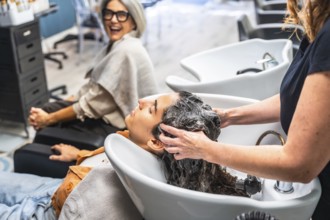 Hairdresser washing customer's hair at basin, providing relaxing care while another woman smiles